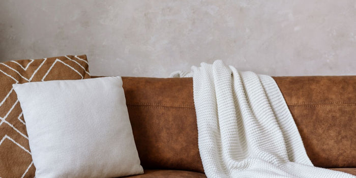 A white throw and cushions on leather sofa